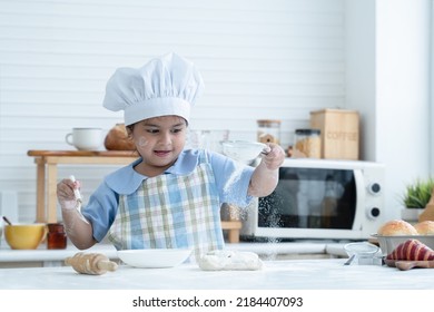 Asian Little Cute Kid Girl Wear Chef Hat And Apron With Flour Mess Up On Face Have Fun Sifting Flour On Dough Bread In Kitchen At Home Or Baking Class At School. Child Education Concept