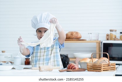 Asian Little Cute Kid Girl Wear Chef Hat And Apron With Flour Mess Up On Face Showing Dough Bread She Knead By Hands And Rolling Pin At Kitchen Home Or Baking Class At School. Child Education Concept