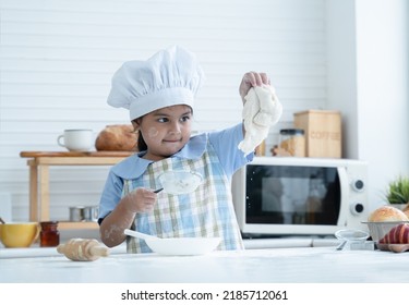 Asian Little Cute Kid Girl Wear Chef Hat And Apron With Flour Mess Up On Face Have Fun Sifting Flour And Knead Dough Bread In Kitchen At Home Or Baking Class At School. Child Education Concept