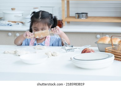 Asian Little Cute Kid Girl Wear Apron With Flour Mess Up On Face And Arms Holding Wooden Rolling Pin Kneading Dough Bread At Kitchen Home Or Baking Class At School. Child Education Concept