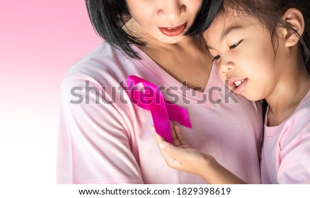 Asian Little daughter and mother embrace together .Daughter holds a pink ribbon attached on her mother's chest tenderly, breast cancer awareness symbol, cancer survivor.