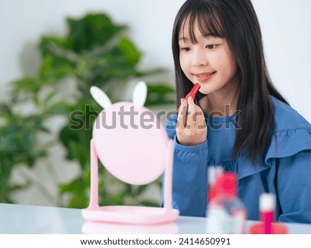 Asian little girl applying a lipstick. Kids cosmetics.