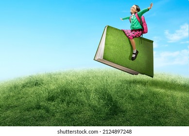 Asian little girl with eyeglasses sitting on a flying book. World Book Day
