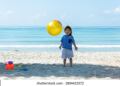 Asian Little Girl Have Fun And Play Yellow Ball On The Beach.  Family Kid Tourism Travel Enjoy And Freedom In Summer And Holiday For Leisure And Destination. Travel And Family Concept