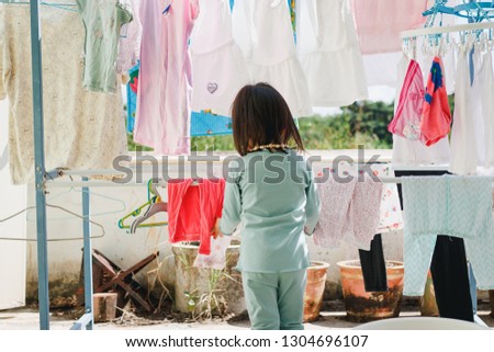 Asian little girl helps her mother to hang up clothes.