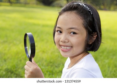 Asian Little Girl Holding A Magnifying Glass In Outdoor