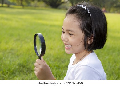 Asian Little Girl Holding A Magnifying Glass In The Park