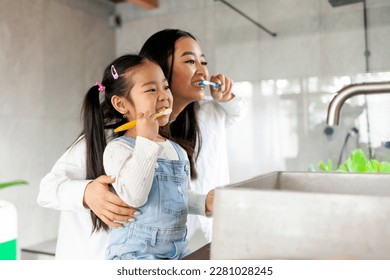 asian little girl with mom brushing teeth in bathroom, korean woman helping to brush daughter's teeth at home together, asian family and hygiene procedures - Powered by Shutterstock