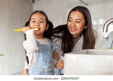 asian little girl with mom brushing teeth in bathroom, korean woman helping to brush daughter's teeth at home together, asian family and hygiene procedures