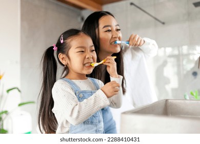 asian little girl with mom brushing teeth in bathroom, korean woman helping to brush daughter's teeth at home together, asian family and hygiene procedures - Powered by Shutterstock