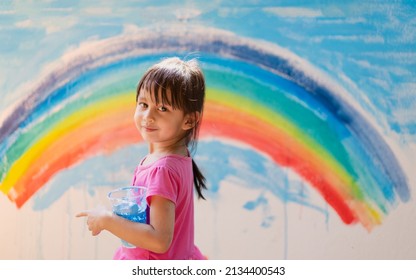 Asian Little Girl Is Painting The Colorful Rainbow And Sky On The Wall And She Look Happy And Funny, Concept Of Art Education And Learn Through Play Activity For Kid Development.	