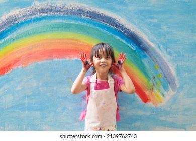 Asian Little Girl Is Painting The Colorful Rainbow And Sky On The Wall And She Look Happy And Funny, Concept Of Art Education And Learn Through Play Activity For Kid Development.