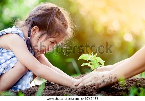 Asian little girl and parent planting young tree on black soil together as save world concept in vintage color tone