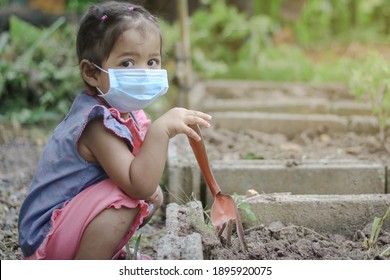 Asian Little Girl Is Planting The Plant In The Garden And Wearing Surgical Mask Outside The House, Concept Of Dust PM 2.5, Covid-19, Coronavirus Protection. 