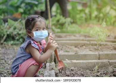 Asian Little Girl Is Planting The Plant In The Garden And Wearing Surgical Mask Outside The House, Concept Of Dust PM 2.5, Covid-19, Coronavirus Protection. 