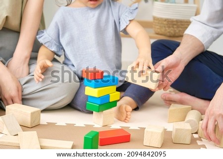 Asian little girl playing with building blocks with her parents, no face