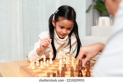 Asian Little Girl Is Playing Chess Board Game Withe Father In The Living Room With Happy Moment. Concept Of Kid Learning, Strategy, Education, Friendship, Competition, Lose And Win.