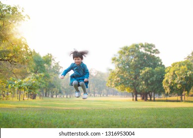 Asian little girl playing having fun and jumping on the grass in park, beautiful summer day