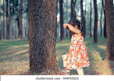 Asian little girl is playing hide-and-seek hiding face in the park