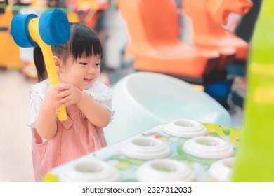 Asian little girl playing whack a mole arcade game at  amusement park, She happy and enjoy, Learning and active of kids concept.