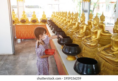 Asian Little Girl Put Mask And Make Merit At The Temple. Buddhist Make Merit, Pay Coins