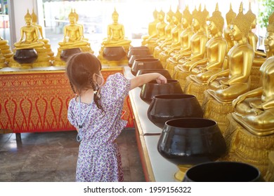 Asian Little Girl Put Mask And Make Merit At The Temple. Buddhist Make Merit, Pay Coins