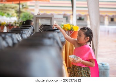 Asian Little Girl Put Mask And Make Merit At The Temple. Buddhist Make Merit, Pay Coins.