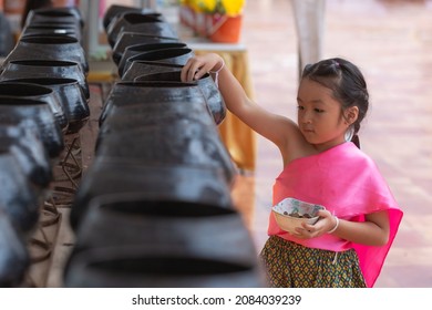 Asian Little Girl Put Mask And Make Merit At The Temple. Buddhist Make Merit, Pay Coins.