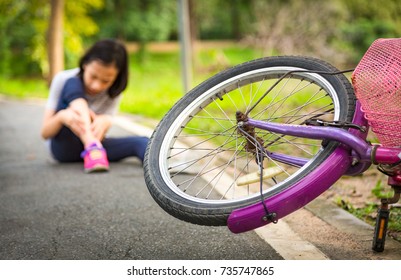 Asian Little Girl Sitting Down On The Road With A Leg Pain Due To A Bicycle Accident, The Bike Fall In Front Of The Child At The Park,Accident Concept