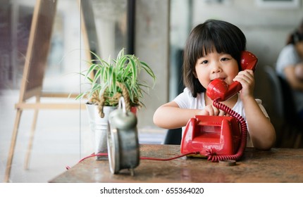 Asian little girl Talking on vintage red telephone.