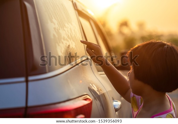 Asian little\
girl writing or drawing star symbol on wet mirror of her father SUV\
car in morning for love\
concept