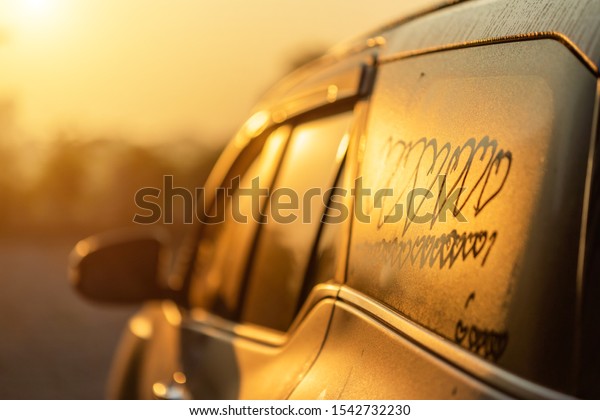Asian little\
girl writing or drawing heart symbol on wet mirror of her father\
SUV car in morning for love\
concept