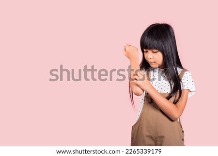 Asian little kid 10 years old scratching itch arm from a mosquito bite at studio shot isolated on pink background, Portrait of Happy child girl dermatitis and scabies, Allergy symptoms, malaria day