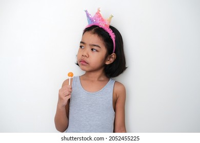 Asian Little Kid Glancing To Her Side With Annoyed Face Expression While Holding Lolipop Candy 