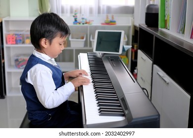 Asian Little Kid Learning Piano Online At Home With Digital Tablet.