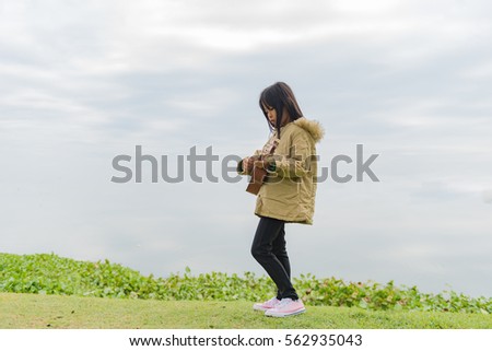 Asian little kids girl sitting on grass and play ukulele in park
