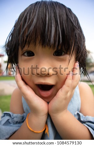 Asian little playful girl rests her chin on hands and open mouth