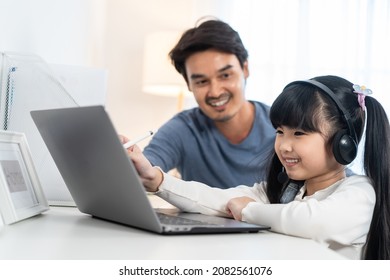 Asian Little Young Girl Kid Learning Online Class At Home With Father. Preschool Child Use Laptop Computer Do Homework, Homeschool From School Teacher By Digital Remote Internet With Support From Dad.