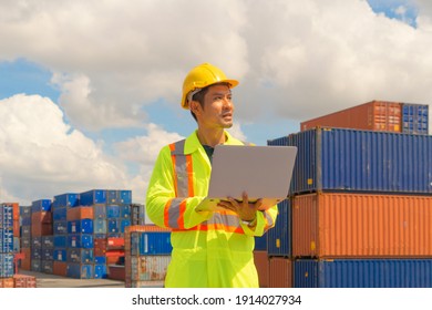 Asian Logistic Worker Engineer Man Using A Laptop Computer, Working In Cargo Container Warehouse Industry Factory Site In Export, Import, And Transportation Concept. Business People. Technology Device