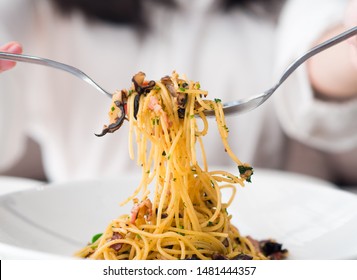 Asian long hair girl eating tasty Italian spaghetti on white plate. Parsley herb, crisp bacon, spice garnished on top dish in modern restaurant. Left right hand hold silverware spoon folk lift up food