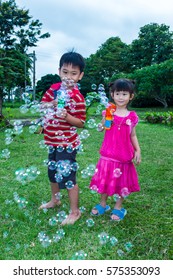 Asian lovely brother and sister smiling and playing together with soap bubbles gun at yard. Outdoor at the daytime with bright sunlight on summer day. Happy family on summer vacation concept.