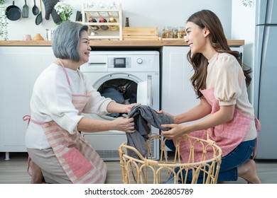 Asian Lovely Family Doing House Working And Chores In Kitchen At Home. Young Girl Daughter Help And Support Senior Old Mother Put Clothes In Washing Machine For Laundry. Housekeeping And Clean Concept