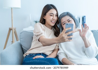 Asian Lovely Family, Young Daughter Use Phone Selfie With Older Mother. Beautiful Girl And Senior Elderly Woman Sit On Sofa, Enjoy Video Call By Internet Online Talking Together In Living Room At Home