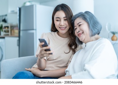 Asian Lovely Family, Young Daughter Use Phone Selfie With Older Mother. Beautiful Girl And Senior Elderly Woman Sit On Sofa, Enjoy Video Call By Internet Online Talking Together In Living Room At Home