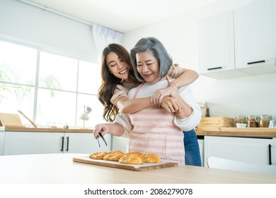 Asian lovely family, young daughter look to old mother cook in kitchen. Beautiful female enjoy spend leisure time and hugging senior elderly mom bake croissant on table in house. Activity relationship - Shutterstock ID 2086279078