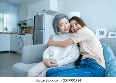 Asian lovely family, young daughter hugging and sit with older mother. Attractive woman granddaughter visit senior elder mature mom in house enjoy spend leisure time together in living room and smile.
