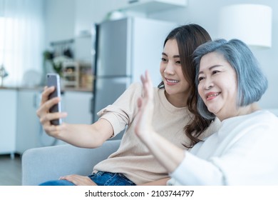 Asian Lovely Family, Young Daughter Use Phone Selfie With Older Mother. Beautiful Girl And Senior Elderly Woman Sit On Sofa, Enjoy Video Call By Internet Online Talking Together In Living Room At Home