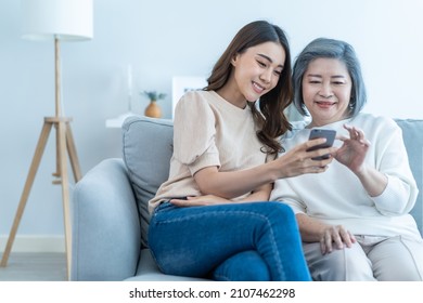 Asian lovely family, young daughter use mobile phone with older mother. Beautiful girl and senior elderly woman sit on sofa, enjoy shopping online on internet website together in living room at home.
