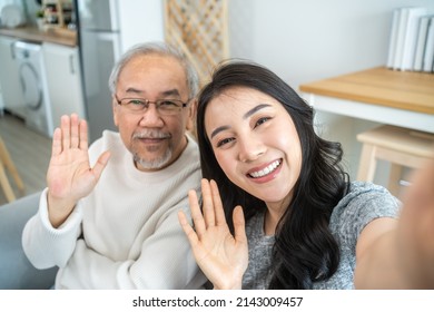 Asian Lovely Family, Young Daughter Use Phone Selfie With Older Father. Beautiful Girl And Senior Elderly Male Sit On Sofa, Enjoy Video Call By Internet Online Talking Together In Living Room At Home.