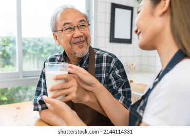 Asian Lovely Family, Young Daughter Prepare Breakfast For Older Father. Attractive Female Wear Apron Bake Bread Serve With Milk To Senior Elderly Dad Sitting On Eating Table In Kitchen At House.